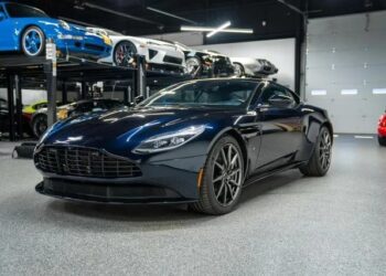 A sleek black Budget Brawn sports car is parked in a showroom, showcasing elegant curves among other cars on lifts in the background.