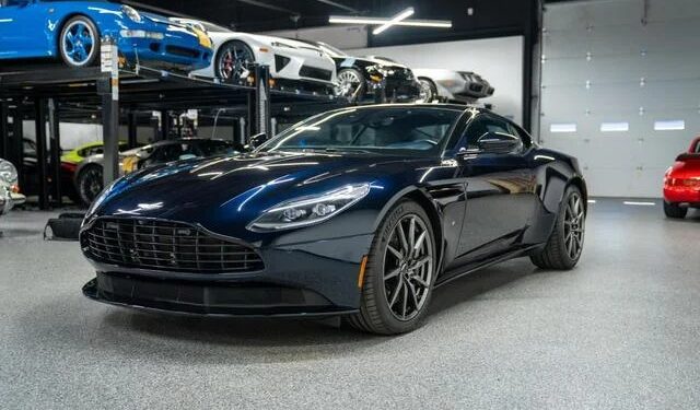 A sleek black Budget Brawn sports car is parked in a showroom, showcasing elegant curves among other cars on lifts in the background.