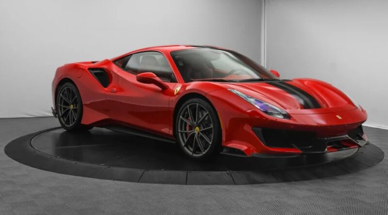 A red Ferrari 488 Pistas with black accents sits on a showroom turntable, exuding its track-ready allure, reminiscent of a prancing horse eager to unleash its power.