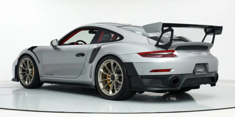 A silver Porsche GT3 RS sports car, known as the ultimate speed machine, features a large rear spoiler and gold alloy wheels, viewed from the rear three-quarter angle in a white studio setting.