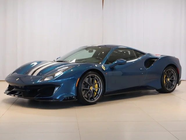 A sleek blue Ferrari sports car with a black stripe on the hood, parked indoors against a white backdrop, showcases its aerodynamic design and vibrant colors, including striking yellow brake calipers. Now available for sale to those who appreciate elegance and performance.