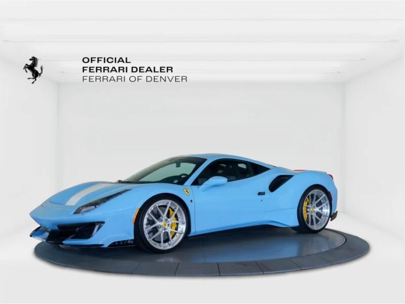 A stunning light blue Ferrari 488 Pistas, with the iconic Prancing Horse emblem, is elegantly displayed in the showroom. The sign reads "Official Ferrari Dealer, Ferrari of Denver," indicating this masterpiece is for sale.