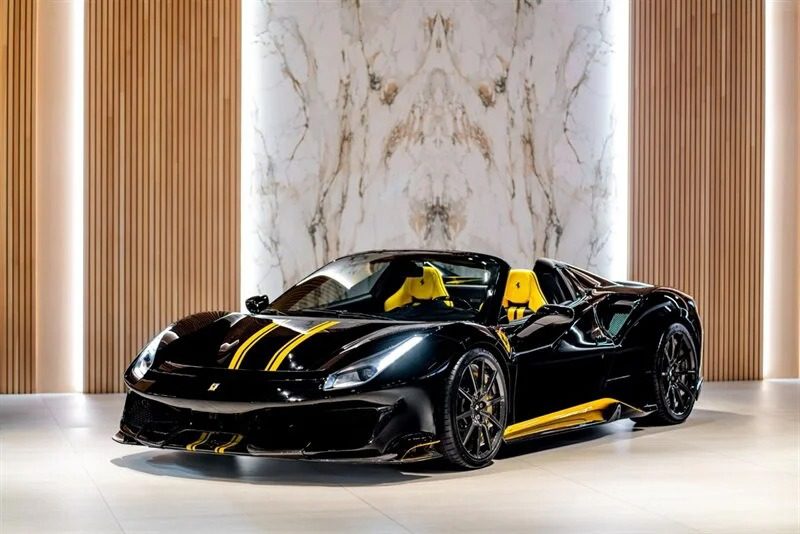 A black and yellow Ferrari 488 Pista with a sleek design is displayed indoors against a marble and wood-paneled backdrop.