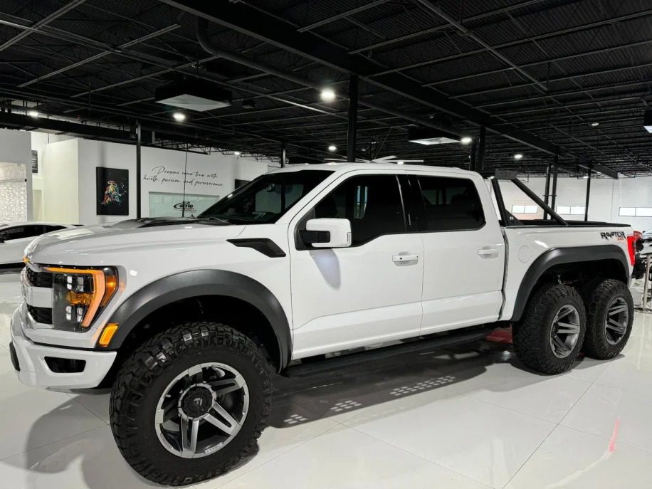 A white 6x6 truck stands proudly on display in the indoor showroom, ready to turn heads.