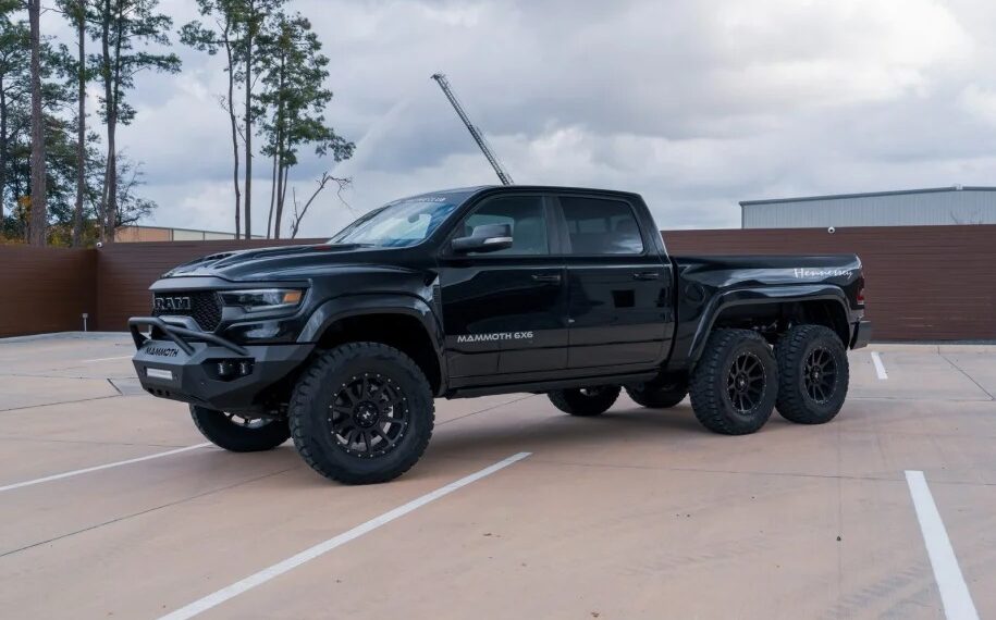 A black 6x6 pickup truck parked in an empty lot with trees and a cloudy sky in the background is sure to turn heads.