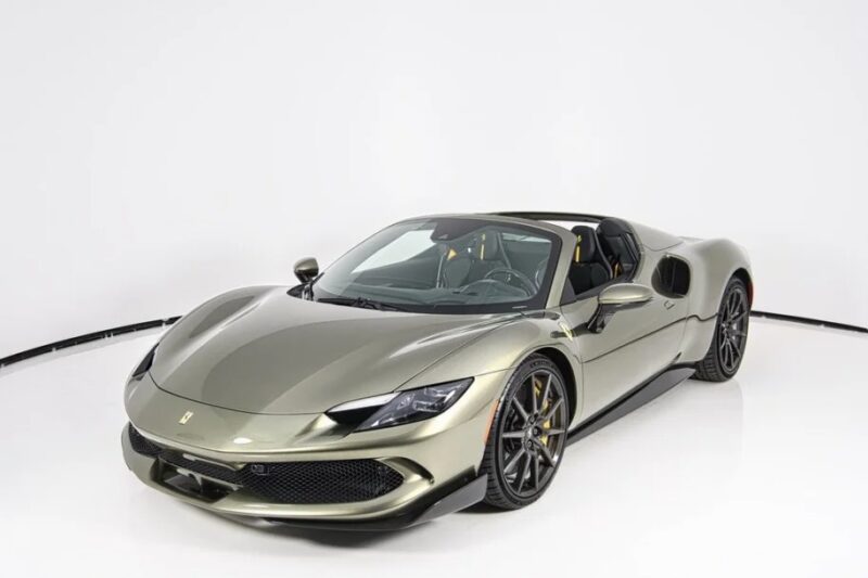 A sleek metallic gray sports car, reminiscent of a Ferrari, is parked indoors on a white background, showcasing its aerodynamic design and black alloy wheels.