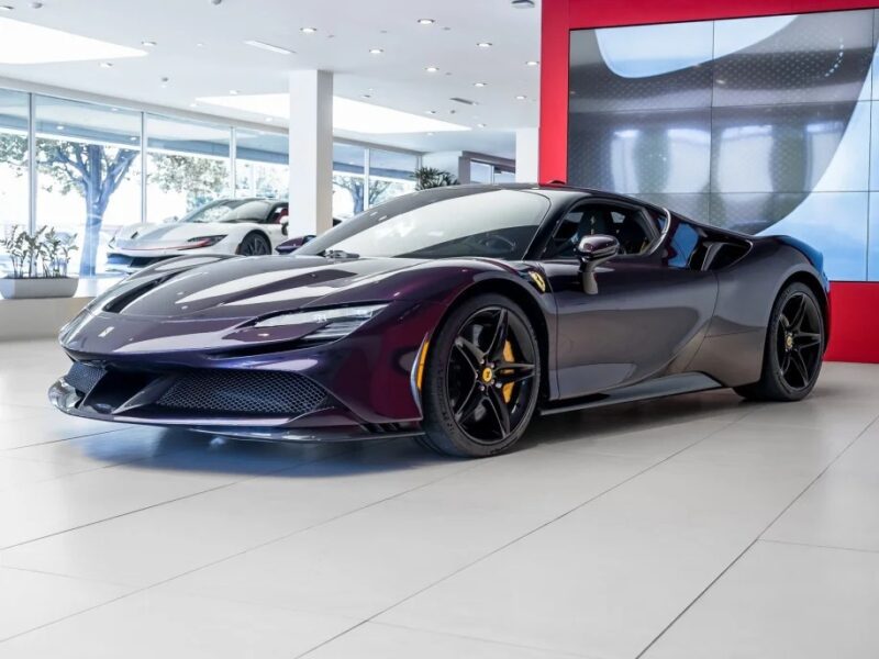 A sleek, dark purple Ferrari sports car is showcased in a modern showroom with a red accent wall and large windows, highlighting its stunning colors. Don't miss the opportunity to own this masterpiece now on sale.