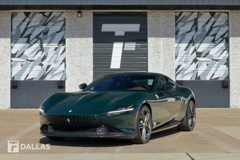 A sleek green Ferrari sports car is parked in front of a modern garage with large doors, featuring geometric designs and a "T" logo, showcasing an impressive fusion of colors.