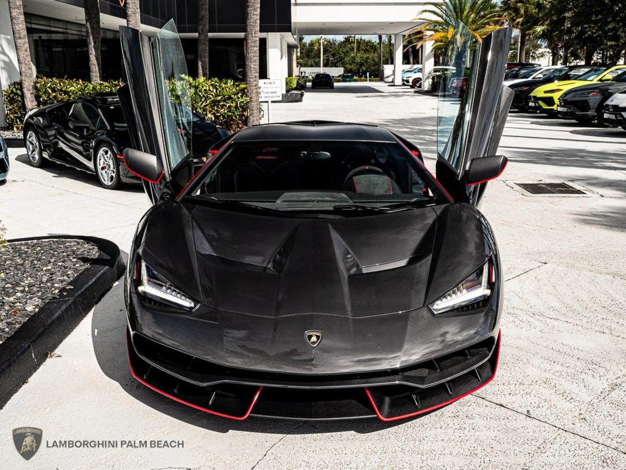 A sleek black Lamborghini Centenario with scissor doors open glistens under the sun, parked amidst palm trees and other vehicles. The scene exudes luxury reminiscent of a Giallo Midas masterpiece.