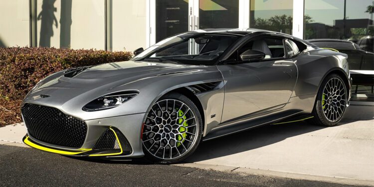 A silver sports car with neon yellow accents is parked in front of a modern glass building on a sunny day, featured in our Dealer Spotlight from Aston Martin Orlando, where exotics for sale redefine luxury and performance.