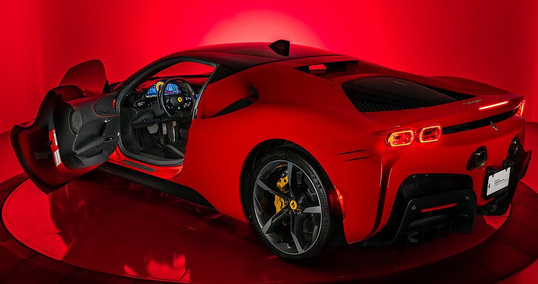 Red sports car with open driver's door, illuminated interior, and sleek design against a vibrant red backdrop. Explore Certified Pre-Owned Ferraris for sale that offer both luxury and peace of mind.