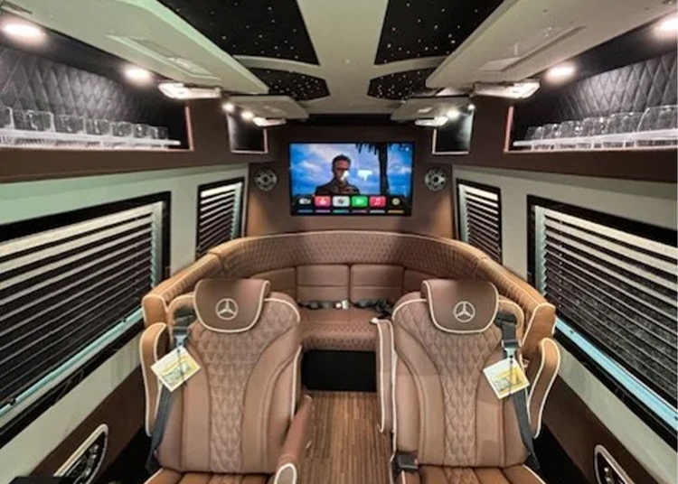 Luxury RVs interior featuring brown leather seating, two front-facing seats with Mercedes logos, a large screen TV, and LED lighting on the ceiling and walls—perfect for those seeking Executive Sprinters or upscale RVs for sale.