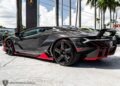 A stunning black and red Lamborghini Centenario is parked outdoors near palm trees, with its iconic logo gleaming in the sun. This exotic beauty is for sale, offering a chance to own a masterpiece of automotive engineering.