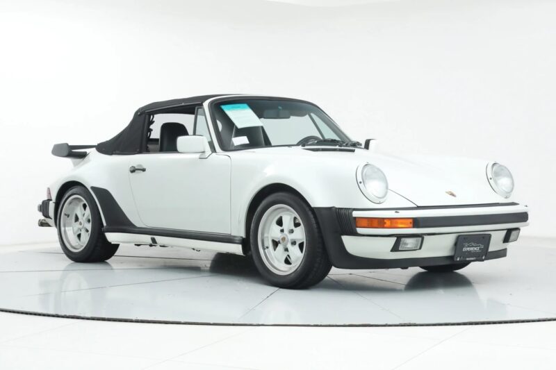 A white Porsche 911 Cabriolet with a black soft top, considered one of the best Air-Cooled Porsches, is parked in a well-lit studio with a plain white background.