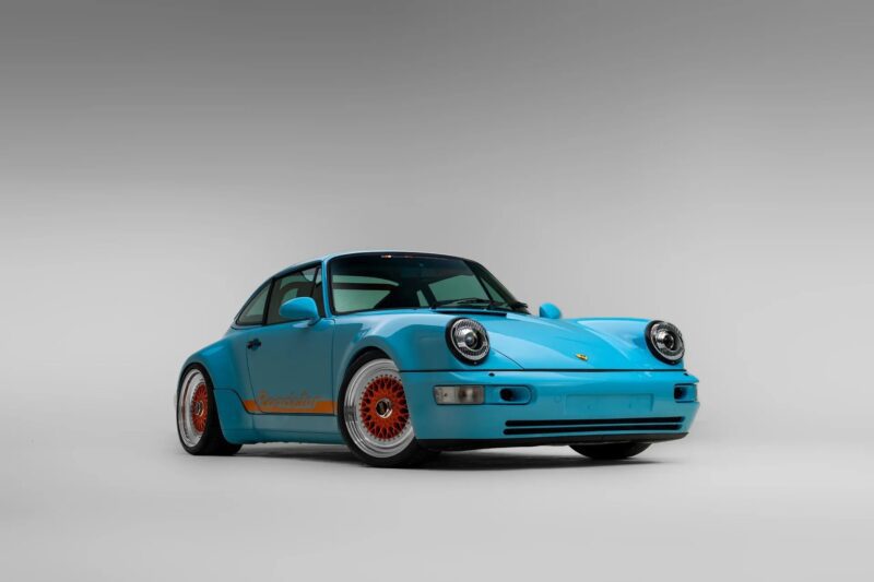 A light blue Porsche sports car with orange wheels and detailing, viewed from the front left against a plain gray background—a striking example among the Best Air-Cooled Porsches.