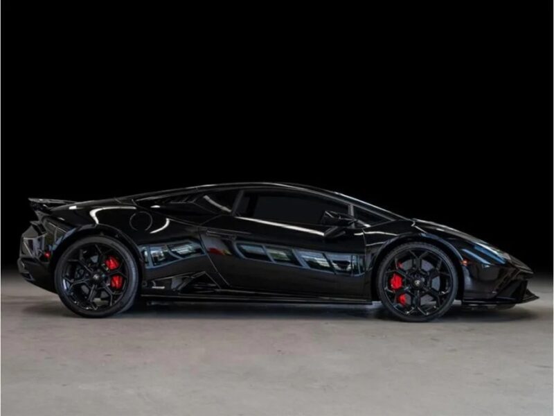 A sleek black V10 supercar, the Lamborghini Huracan with red brake calipers, is shown in profile against a dark background, showcasing its stunning design and performance. For sale now.