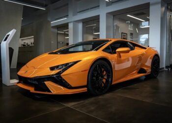 A bright orange Lamborghini Huracan Tecnica, a stunning V10 supercar, is parked indoors on a dark tiled floor.