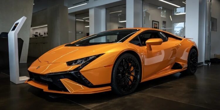 A bright orange Lamborghini Huracan Tecnica, a stunning V10 supercar, is parked indoors on a dark tiled floor.