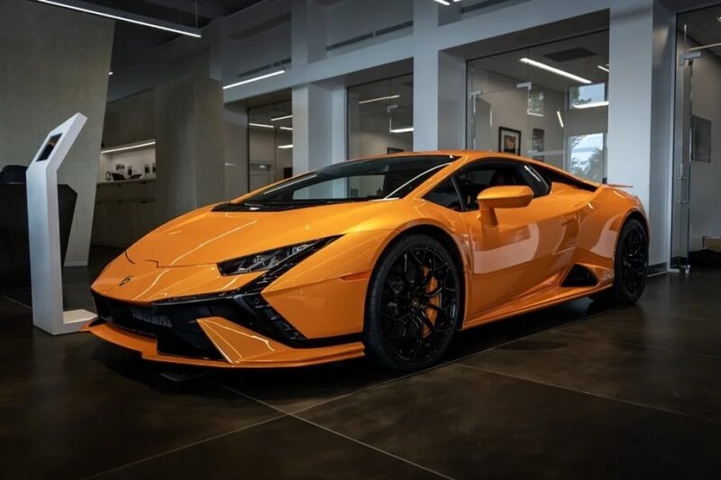 A bright orange Lamborghini Huracan Tecnica, a stunning V10 supercar, is parked indoors on a dark tiled floor.