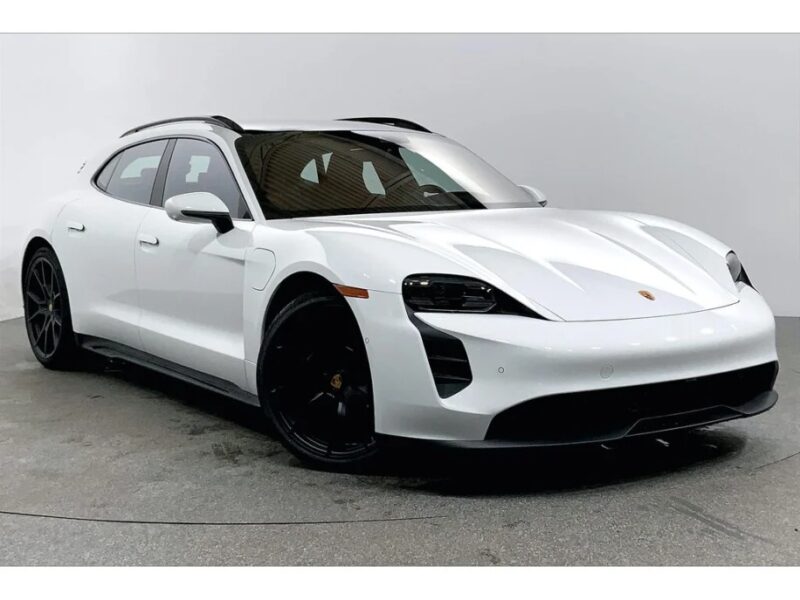 A white, four-door Porsche luxury performance wagon with black wheels is showcased in a studio setting, angled slightly from the front.