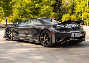 A sleek black sports car, reminiscent of the all-time greats like McLarens, is parked outdoors. It showcases its rear design and aerodynamic features with trees in the background, exuding an aura of luxury and expense.