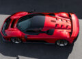 Aerial view of a sleek red Ferrari sports car with a black roof, parked on a gray asphalt surface.