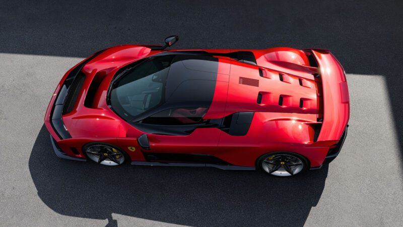 Aerial view of a sleek red Ferrari sports car with a black roof, parked on a gray asphalt surface.