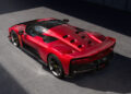 A red Ferrari sports car with a sleek design is parked on a sunlit asphalt surface, viewed from the rear three-quarter angle.