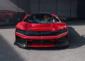 A sleek red Ferrari hypercar is parked majestically in front of a reflective glass wall, its stunning side view perfectly mirrored, emphasizing the car's exquisite design.