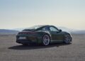 A green 2025 Porsche 911 GT3 sits elegantly on an empty asphalt surface, with majestic mountains in the background.