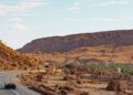 Two hypercars race down a desert highway under a clear sky, with rocky hills and sparse vegetation in the background.