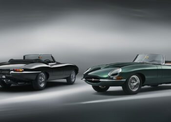 Two classic convertible sports cars, including a sleek black E-Type Jaguar, are parked against a soft-focus gray background.