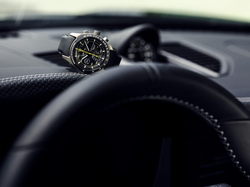 A wristwatch with a black strap rests on the dashboard of a 2025 911 GT3, with the Porsche steering wheel prominently visible in the foreground.