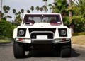 Front view of a sleek 1990 Lamborghini LM002 parked on a road, surrounded by swaying palm trees.