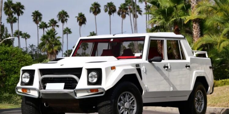A 1990 Lamborghini LM002, an iconic white off-road vehicle, is parked on a street, surrounded by swaying palm trees and lush greenery. This rare Lamborghini for sale brings adventurous spirit and luxury to any terrain.