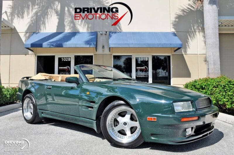 A green convertible, reminiscent of 90s cars, is parked in front of a building beneath the "Driving Emotions" sign.