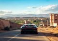 A sleek Bugatti hypercar drives down a rural road in Morocco, with desert landscapes and distant mountains under a clear blue sky.