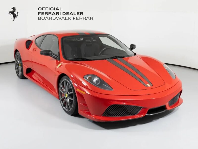 Displayed indoors, the red Ferrari 430 Scuderia with black racing stripes embodies pure speed and luxury. The iconic Prancing Horse proudly signifies its heritage. Text in the top left corner reads "Official Ferrari Dealer Boardwalk Ferrari.