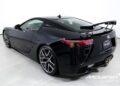 Black Lexus LFA with a rear spoiler parked in a showroom, featuring sleek lines, distinctive tail lights, and a branded floor mat from McLaren Charlotte.