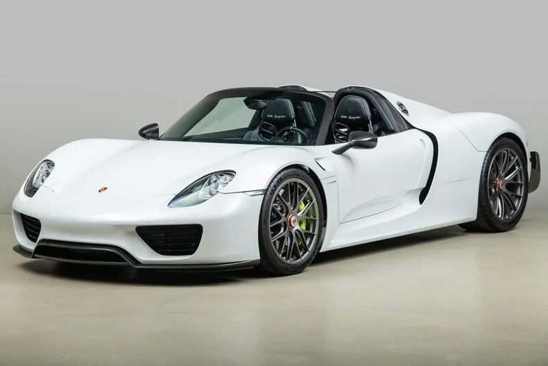 A stunning white Porsche 918 Spyder hypercar is on display against a sleek gray background in the showroom, tempting all who dream to buy Porsche performance.