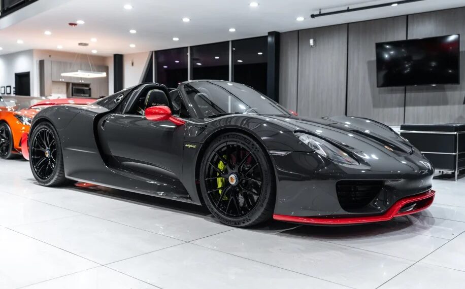 A sleek black Porsche 918 Spyder with red accents is parked indoors. This hypercar features an open top and polished alloy wheels, epitomizing luxury and performance.