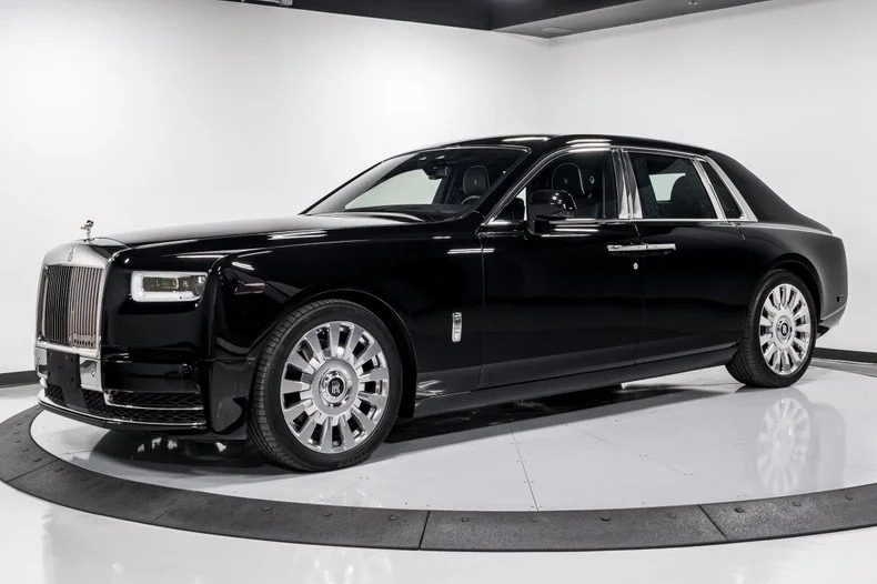 A quintessential Rolls-Royce Phantom luxury sedan is elegantly parked in a pristine, white, well-lit showroom.