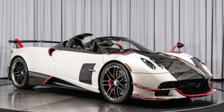 A white and black Pagani Huayra with red accents, featuring an aerodynamic design and convertible roof, is showcased on a rotating platform in the showroom. This stunning Roadster BC is for sale to those who crave elegance and performance.