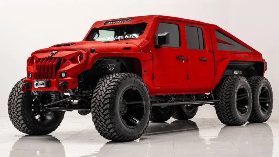 A large, red 6x6 truck with oversized tires and rugged design is parked indoors, sure to turn heads with its robust build and unique styling.