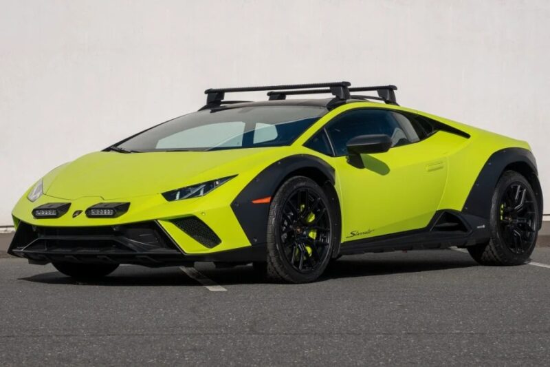 A bright green Lamborghini Huracán Sterrato sports car with a roof rack and black accents is parked on a gray asphalt surface.