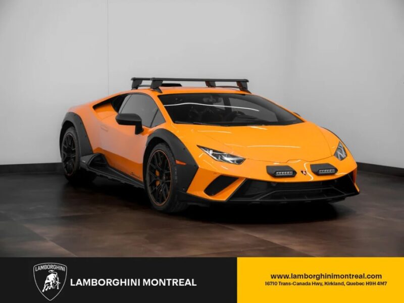 An eye-catching orange Lamborghini Huracán Sterrato with black accents and a roof rack is showcased indoors on a light gray floor. Visit Lamborghini Montreal for more details or to buy your own Huracán Sterrato. Logo and contact details displayed below.