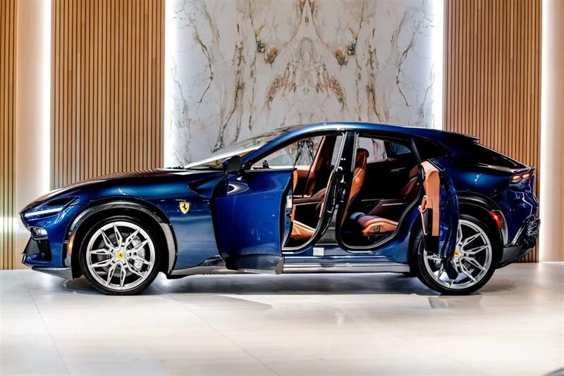 A blue luxury Lamborghini Urus with suicide doors open, revealing a brown leather interior, is displayed in a modern showroom with wood-paneled walls and marble accents.