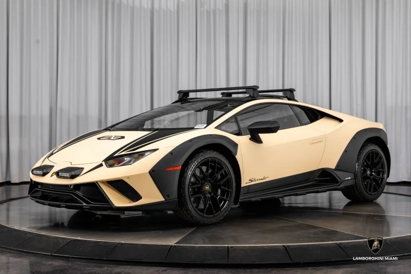 A beige Lamborghini Huracán Sterrato with black accents and a roof rack is elegantly displayed on a circular platform indoors, captivating enthusiasts looking to make a bold Lamborghini purchase.