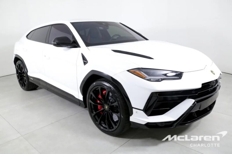 A white Italian Super SUV with black accents and red brake calipers is displayed in a showroom. The vehicle features sporty design elements and is branded with "McLaren Charlotte.