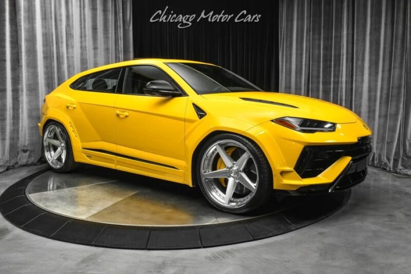 A yellow Lamborghini Urus sits indoors on a turntable, flaunting its sleek design with silver rims and black accents. Above it, "Chicago Motor Cars" commands attention, underscoring the luxurious appeal of this Italian Super SUV.